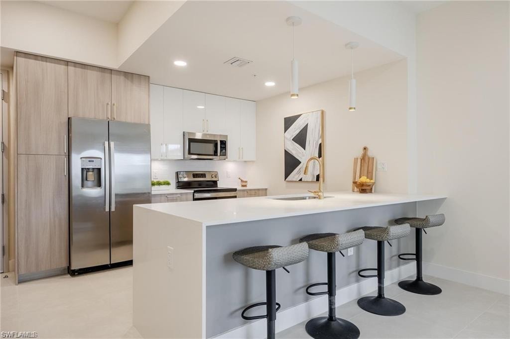 Kitchen featuring recessed lighting, a sink, a peninsula, a kitchen bar, and appliances with stainless steel finishes