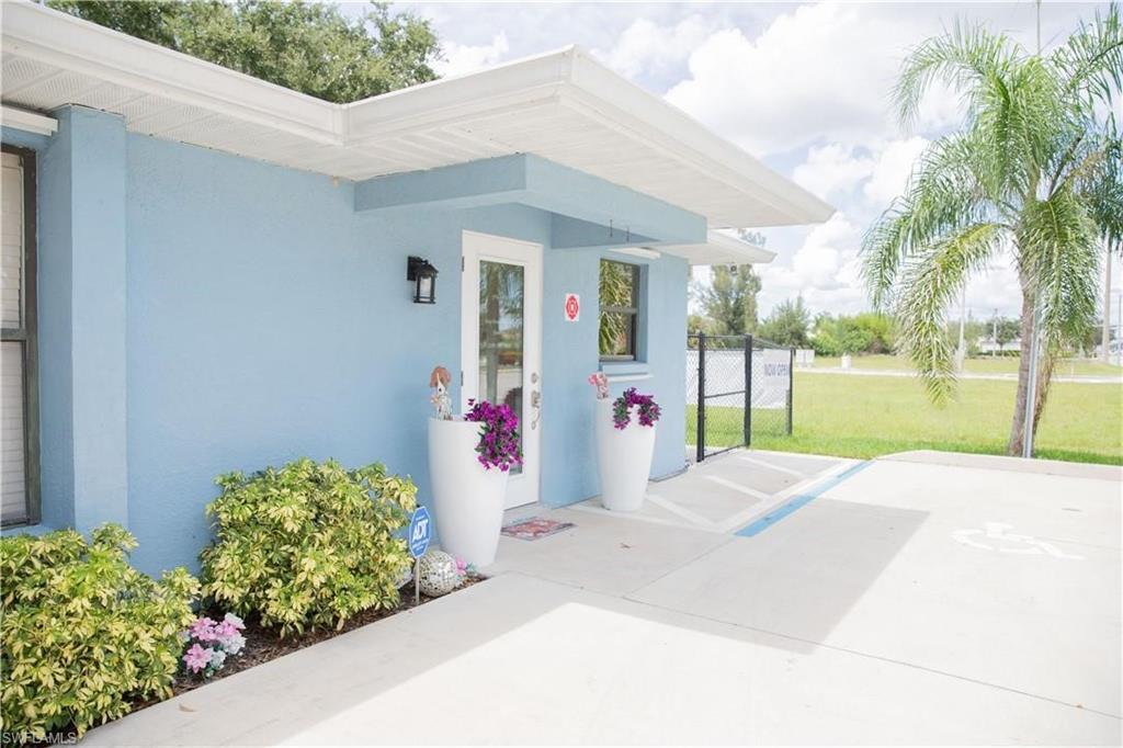 Light blue stucco exterior with white trim, featuring a glass-paneled entry door and an exterior wall light fixture