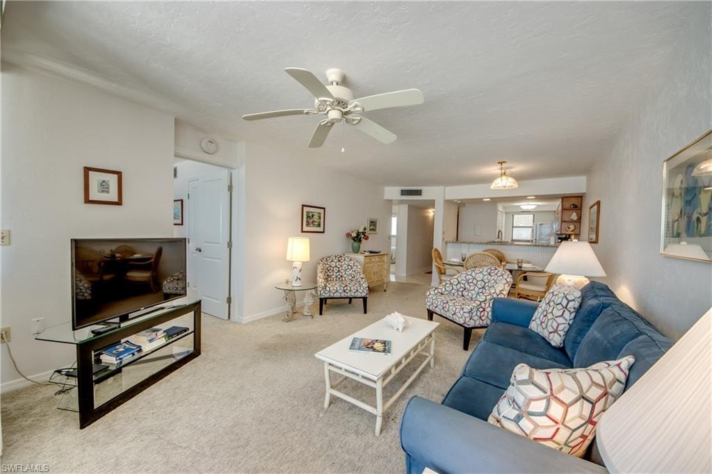 Expansive living area featuring carpet flooring, a ceiling fan, and a pass-through opening to the kitchen