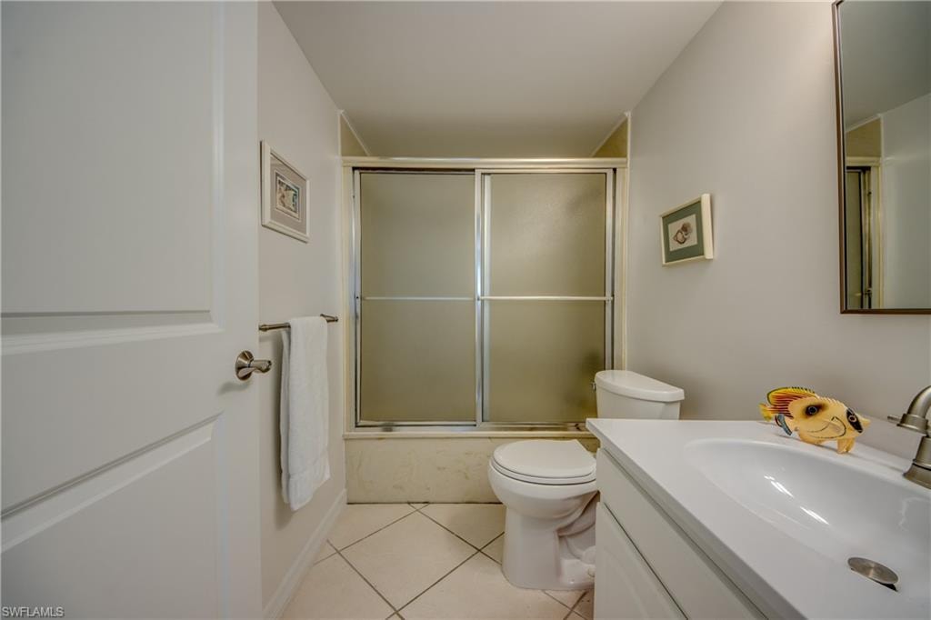 Full bathroom featuring a white vanity with an integrated sink, brushed nickel faucet, a toilet, and a bathtub with frosted glass sliding doors