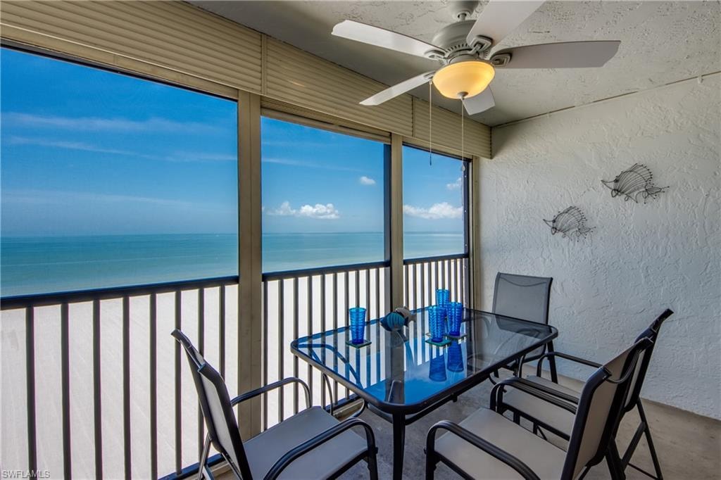 Expansive balcony featuring a white textured wall, ceiling fan with integrated lighting, full-height windows, and a black railing overlooking the ocean