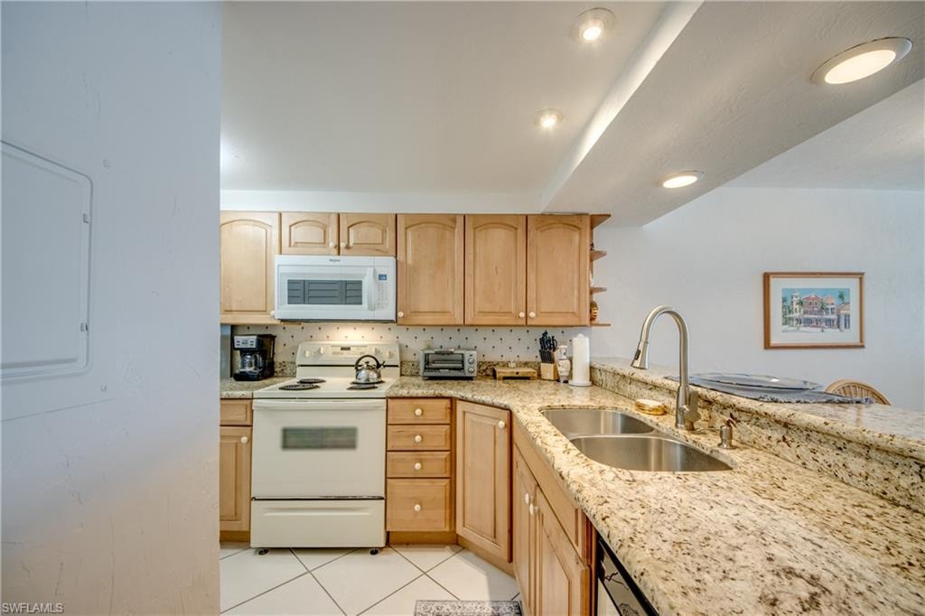 Kitchen featuring light wood cabinetry, granite-style countertops, stainless steel double basin sink with gooseneck faucet, white built-in microwave, and tile flooring