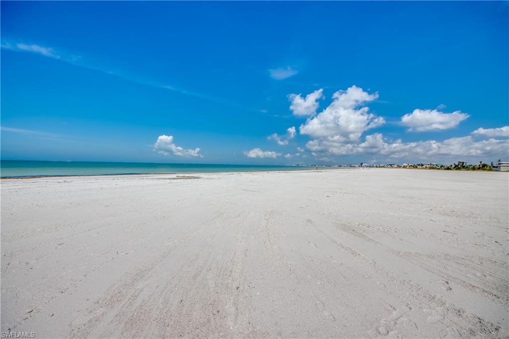 Expansive sandy beach with a clear blue sky, featuring distant coastal structures and calm turquoise waters
