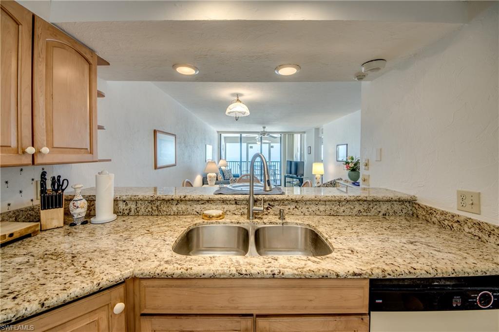 Kitchen featuring L-shaped granite-finish countertops, a double basin stainless steel sink with a high-arch faucet, recessed lighting, wood-finish cabinetry, and a built-in dishwasher