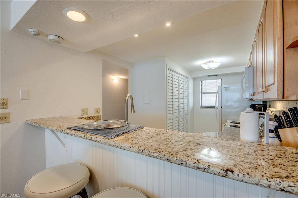 Kitchen featuring a granite-finish countertop, stainless steel sink with gooseneck faucet, light wood cabinetry, and recessed lighting