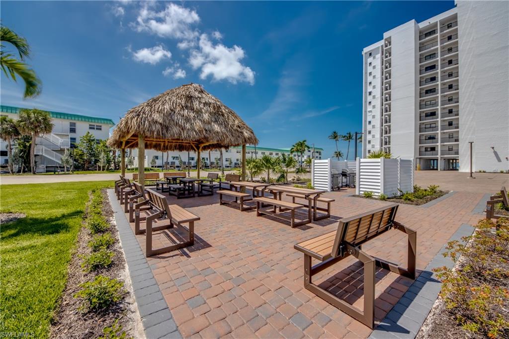 Outdoor common area featuring a thatched-roof tiki hut, paver patio, multiple picnic tables, and seating benches