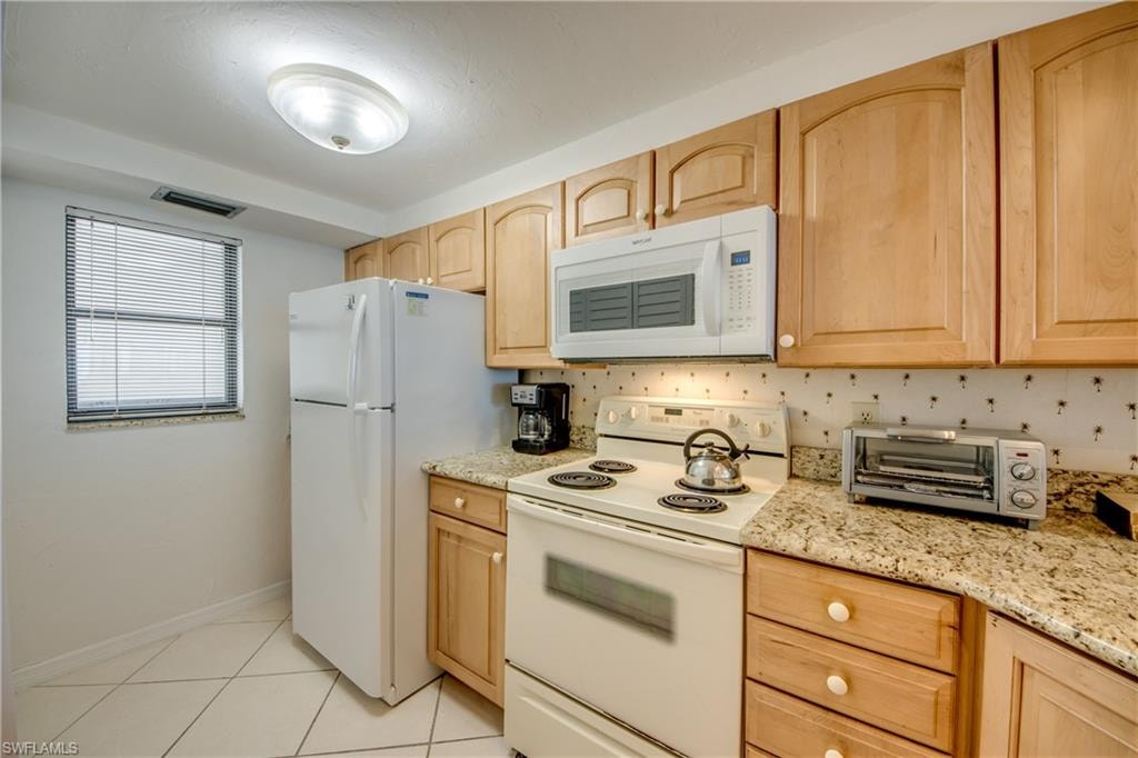 Kitchen featuring a window with horizontal blinds, light-toned cabinetry, white appliances, and granite-style countertops
