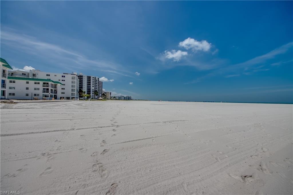 Expansive sandy beach with multi-story buildings, some featuring balconies, under a clear blue sky