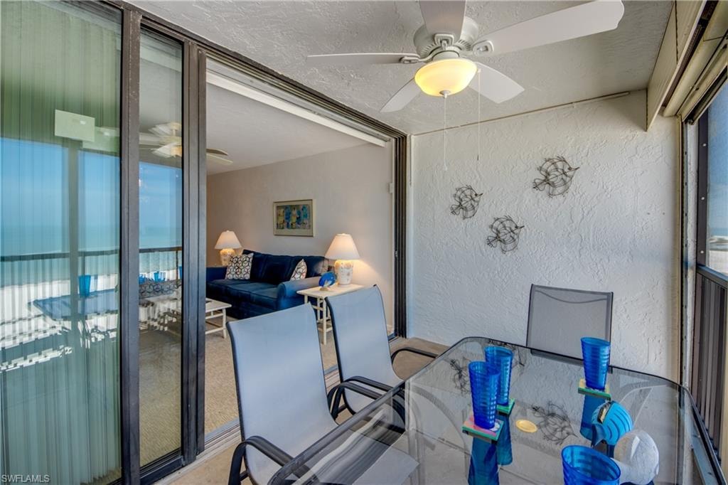 Screened-in balcony with a ceiling fan, glass-top table, and sliding glass doors opening to an interior living space