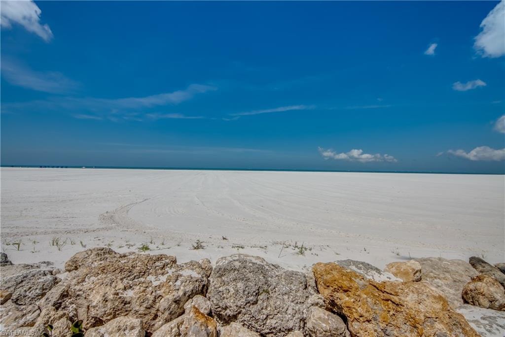 Expansive white sand shoreline extending to the horizon, framed by a clear blue sky and calm waters