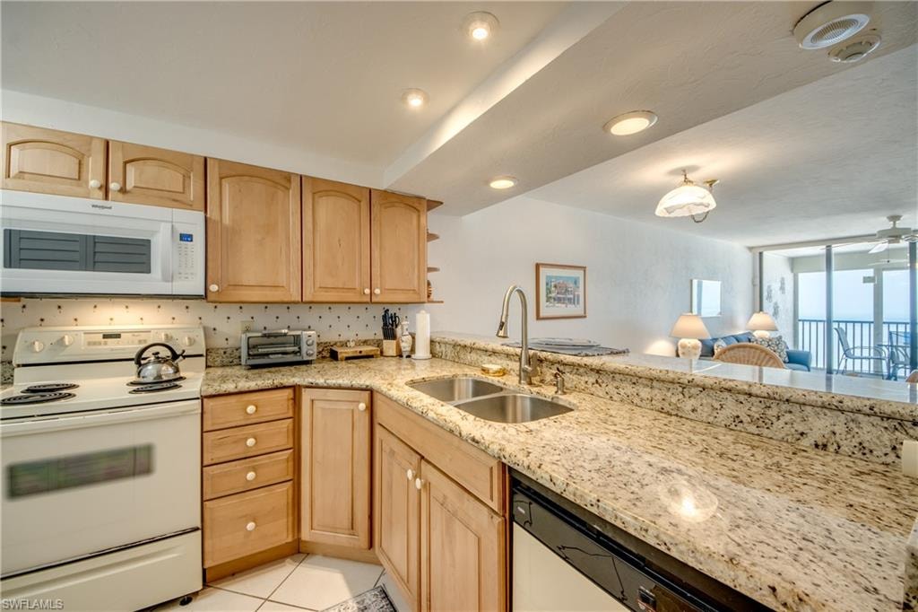 Kitchen featuring light wood cabinetry, stone countertops, double basin sink with gooseneck faucet, and white appliances