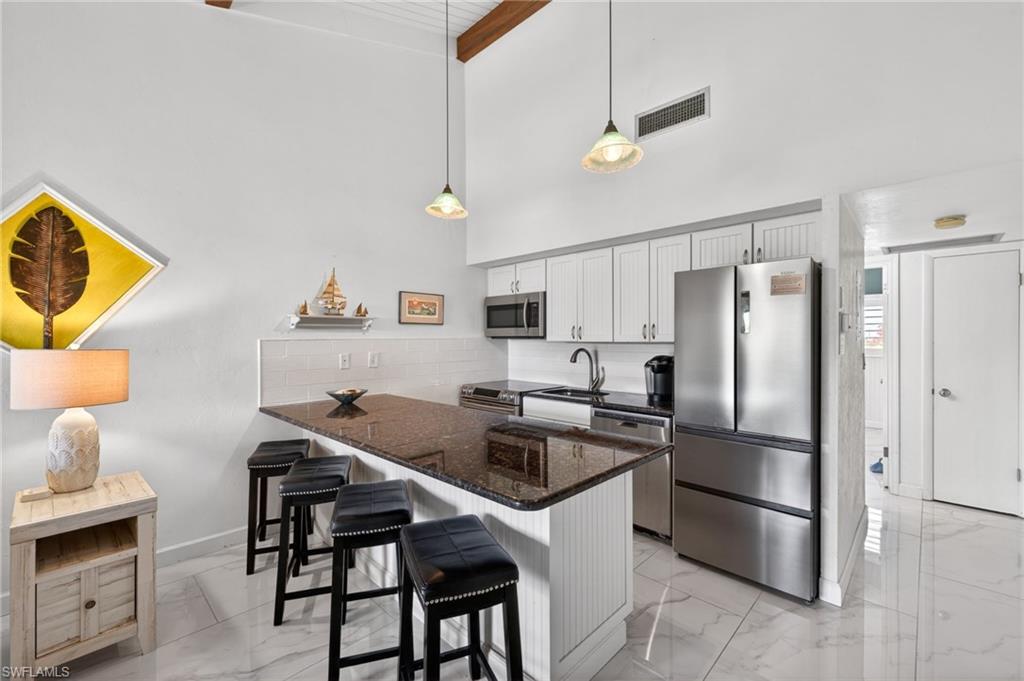 Kitchen featuring a breakfast bar with dark countertop, white shaker-style cabinetry, and stainless steel appliances