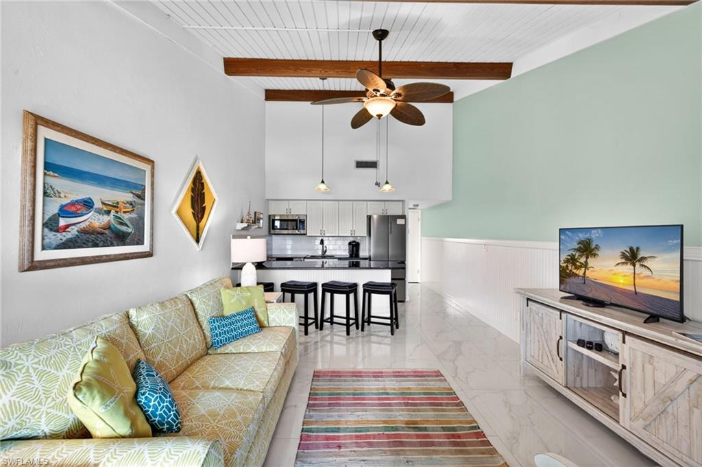 Open-concept living area with high vaulted ceilings, exposed wood beams, and a white plank ceiling