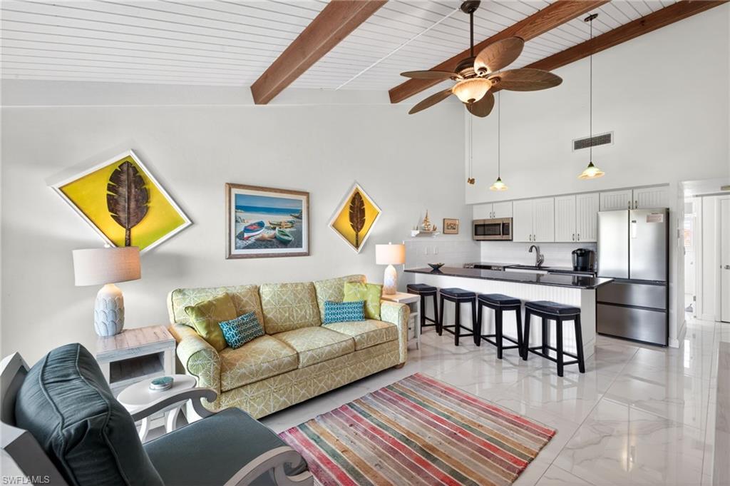 Open-concept living area featuring a vaulted ceiling with exposed wood beams, white wood-finish ceiling panels, and large format tile flooring