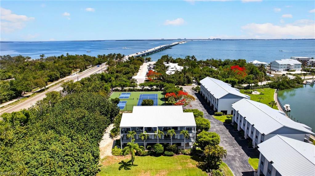 Coastal property featuring multiple buildings with metal roofs, waterside access, a tennis court, and lush tropical landscaping