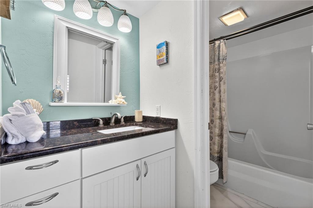 Bathroom featuring a single vanity with a dark countertop and white cabinetry, an undermount sink, and a framed mirror with overhead lighting