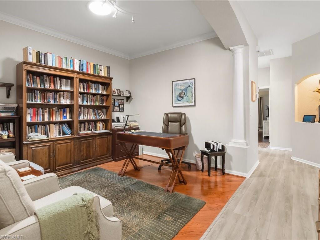 Dedicated room featuring wood-finish flooring, a large built-in bookcase with cabinet storage, crown molding, and a decorative column
