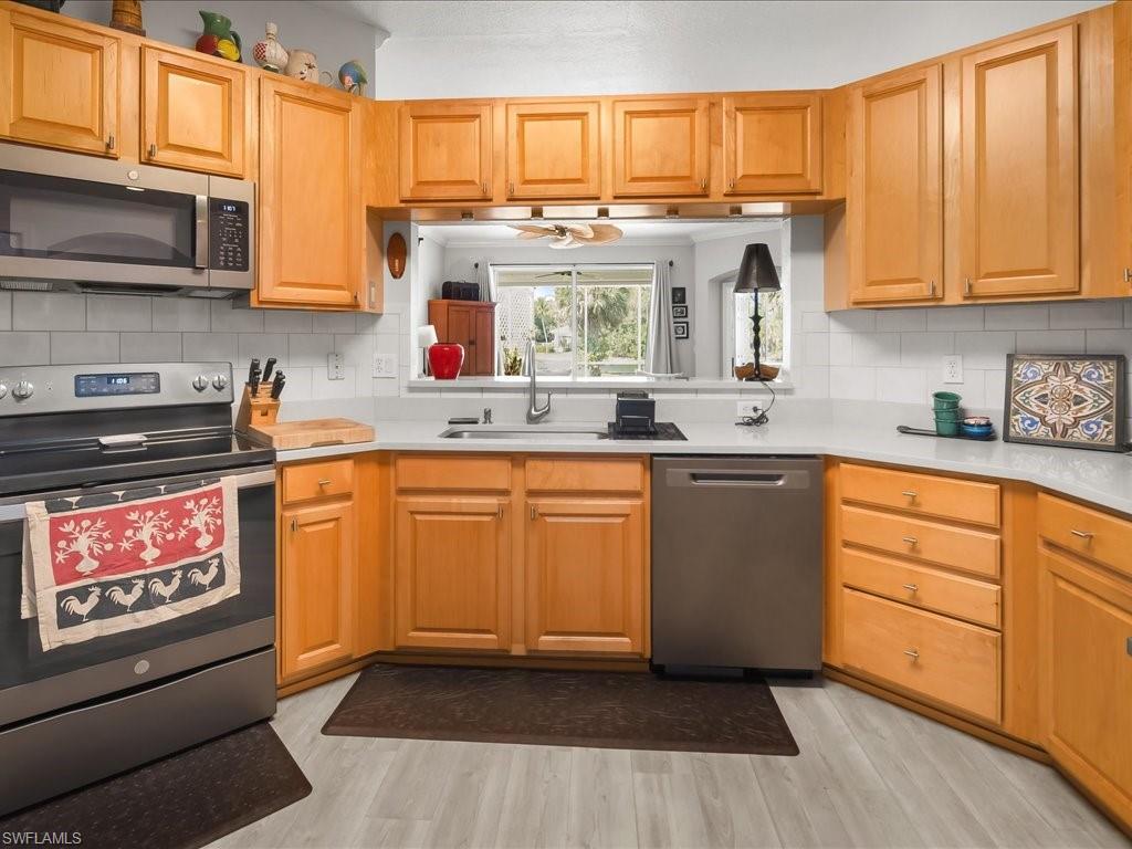 Kitchen featuring light wood cabinetry, stainless steel appliances, a white subway tile backsplash, light-toned countertops, and wood-finish flooring