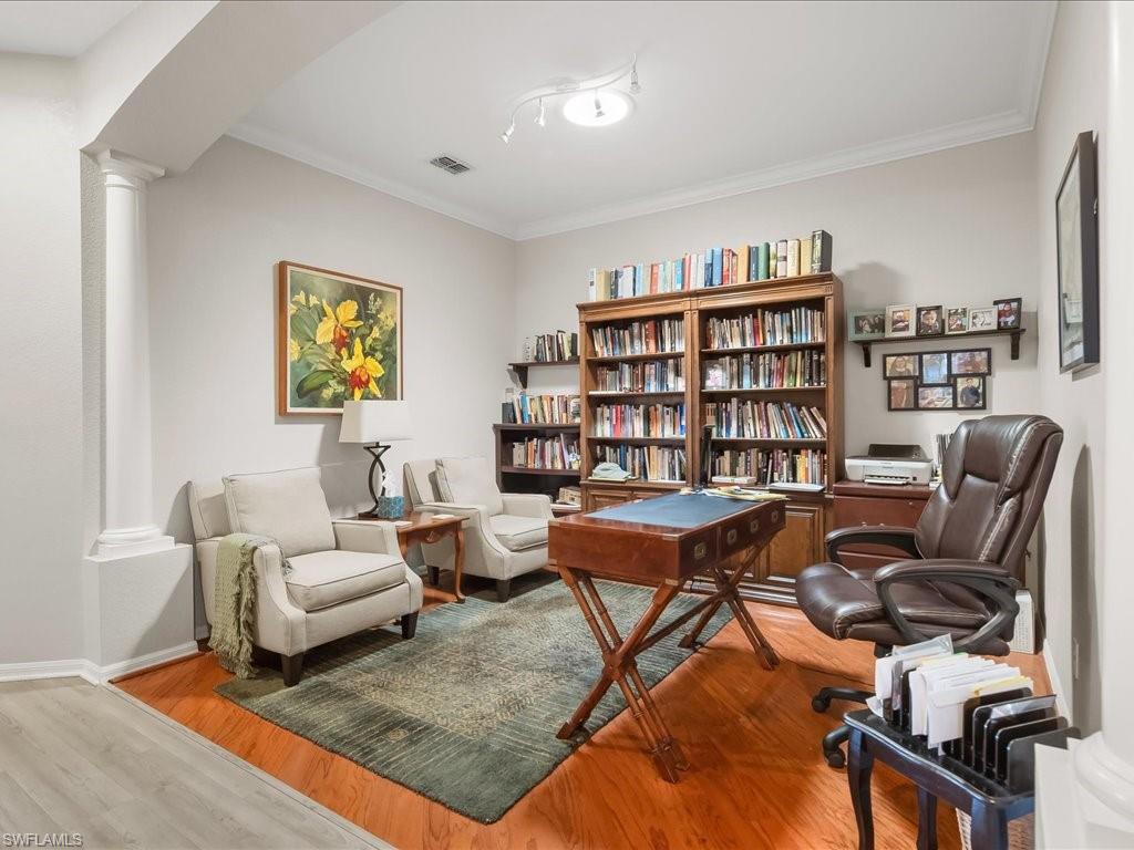 Dedicated study space featuring a decorative column, crown molding, track lighting, wood-finish flooring, and built-in shelving