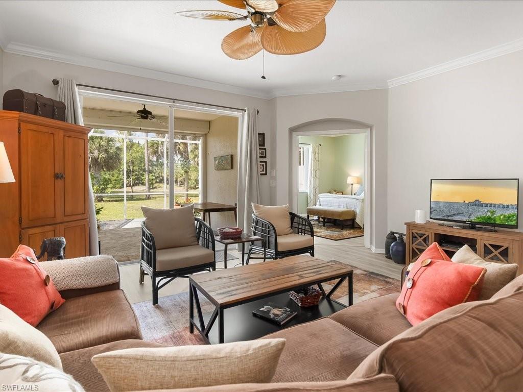 Living area featuring wood-finish flooring, a ceiling fan with palm-leaf blades, and crown molding