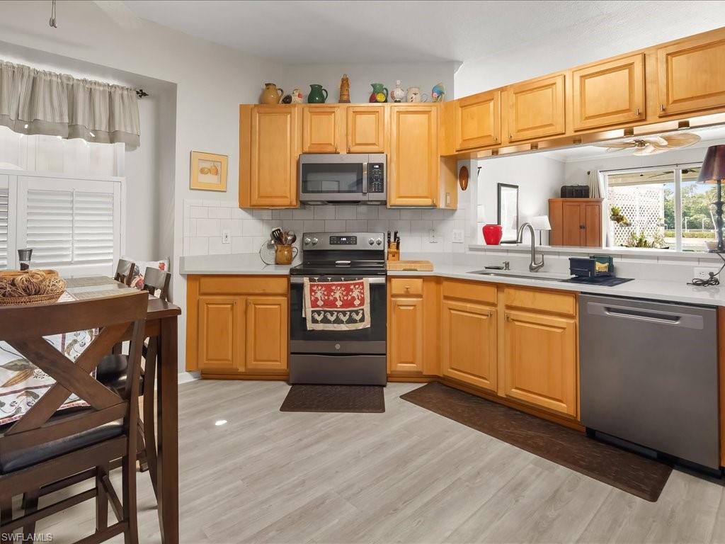 Kitchen featuring wood-finish cabinetry, stainless steel appliances, light-toned countertops, and a white subway tile backsplash