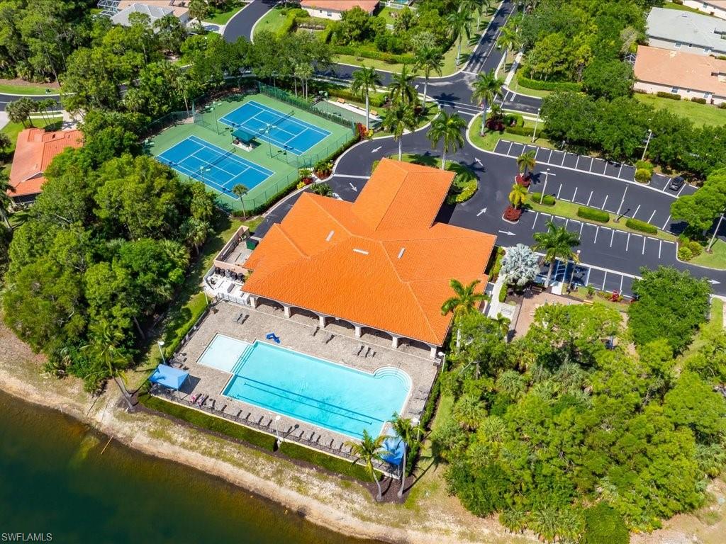 Community recreation building featuring a vibrant orange tile roof, outdoor swimming pool with surrounding lounge areas, and multiple tennis courts