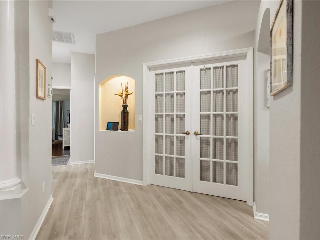 Double French doors with grid-patterned glass, light wood-finish flooring, recessed wall niche, arched doorway, and light wall paint throughout