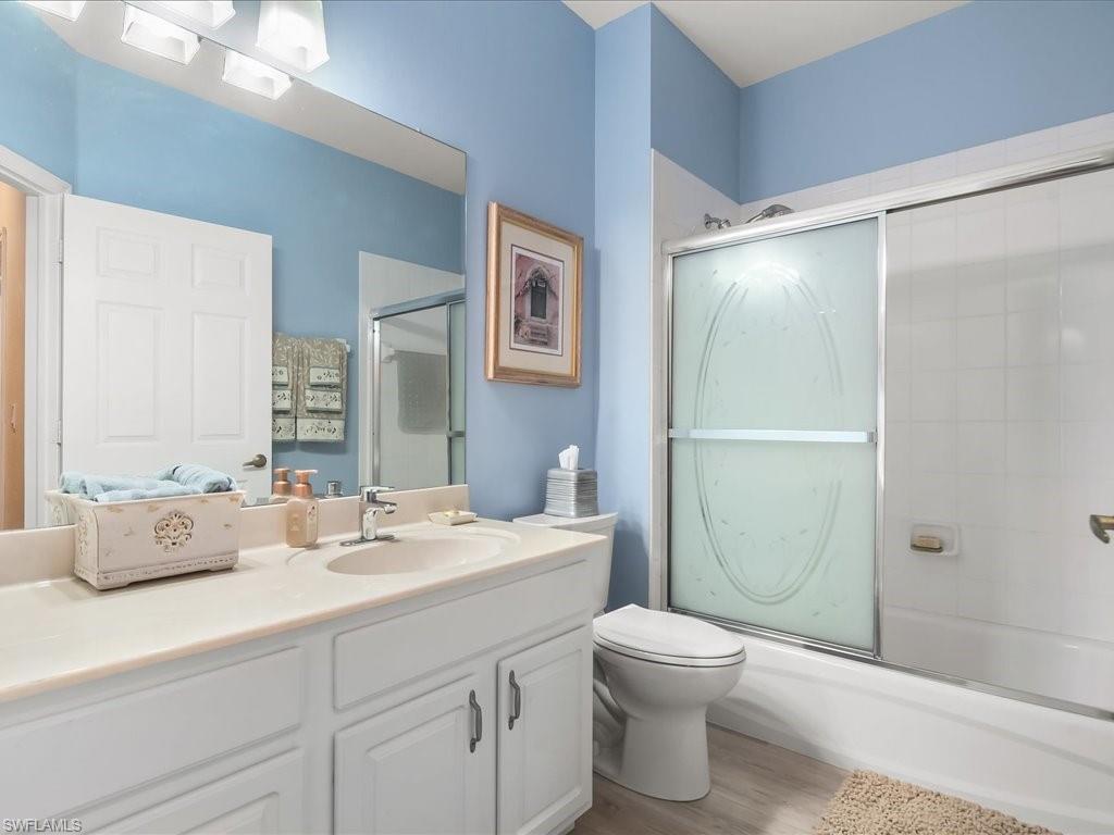 Bathroom featuring a white vanity with integrated sink, a large wall-mounted mirror, white paneled cabinetry, and wood-finish flooring