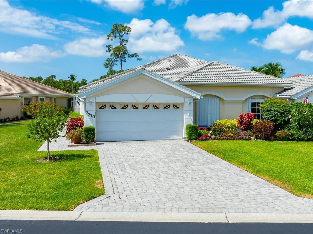 Exterior featuring a paver driveway, an attached two-car garage with transom window accents, a tiled roof, and established landscaping