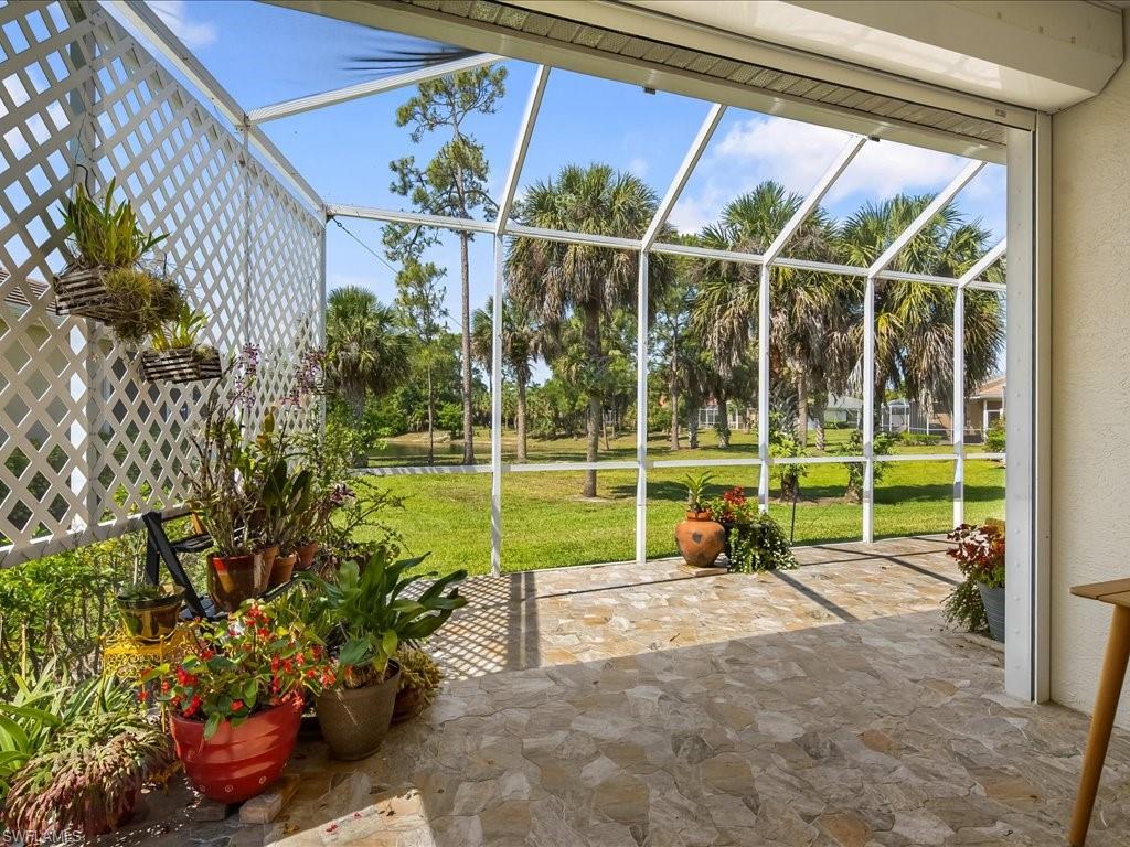 Screened patio featuring a lattice wall, stone-finish flooring, and expansive views of mature palm trees and green space