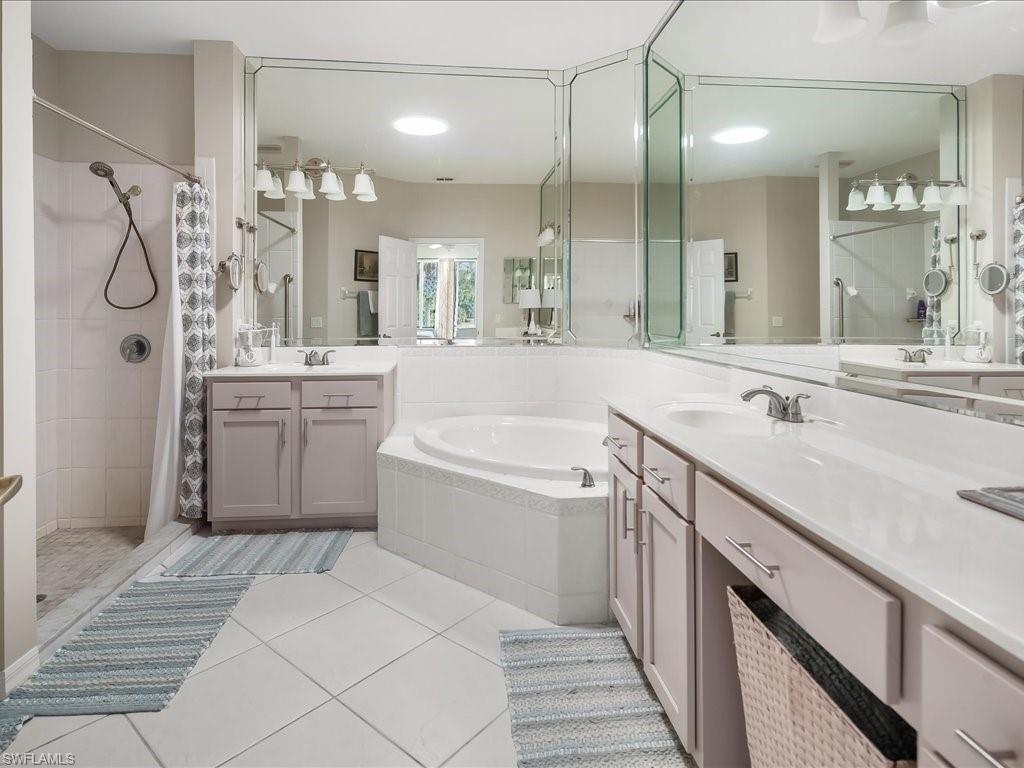 Expansive bathroom featuring a corner soaking tub, dual vanities with light cabinetry, a glass-enclosed shower, and wall-to-wall mirrors