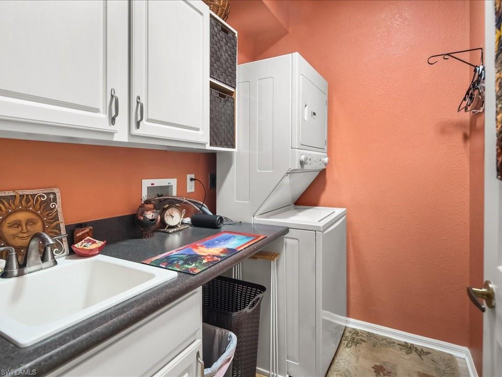 Laundry area featuring a utility sink, dark countertop, white cabinetry, and stacked appliances