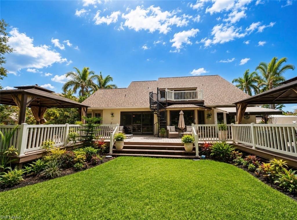Expansive green lawn with surrounding landscaping, multi-level composite decking, white picket railings, and two covered gazebos