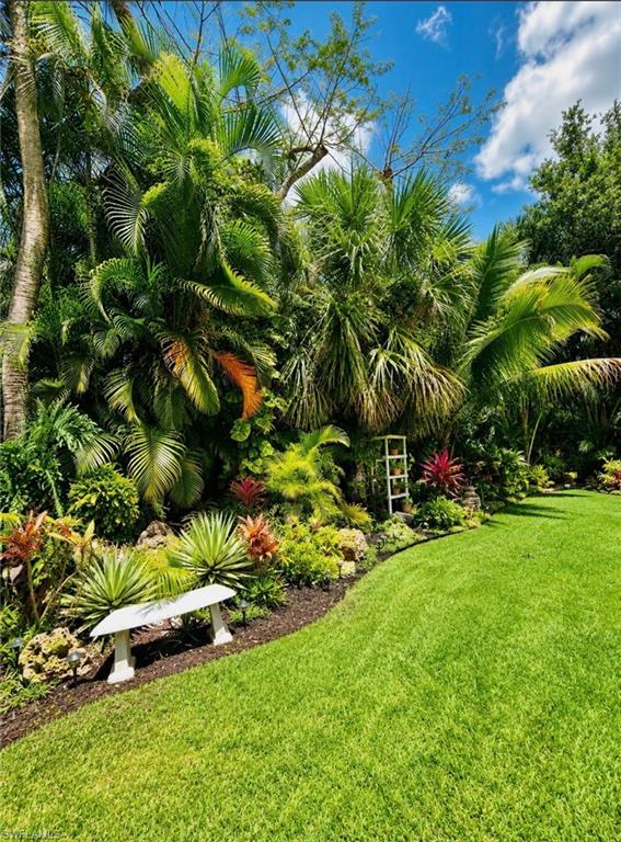 Lush tropical landscaping, expansive grassy area, and a garden bench