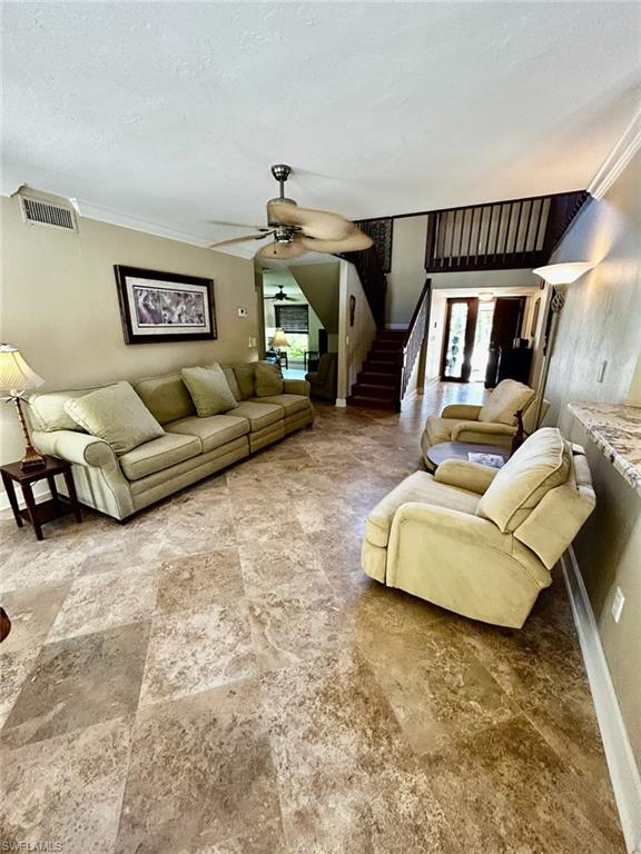 Spacious living area featuring large format tile flooring, crown molding, and a ceiling fan
