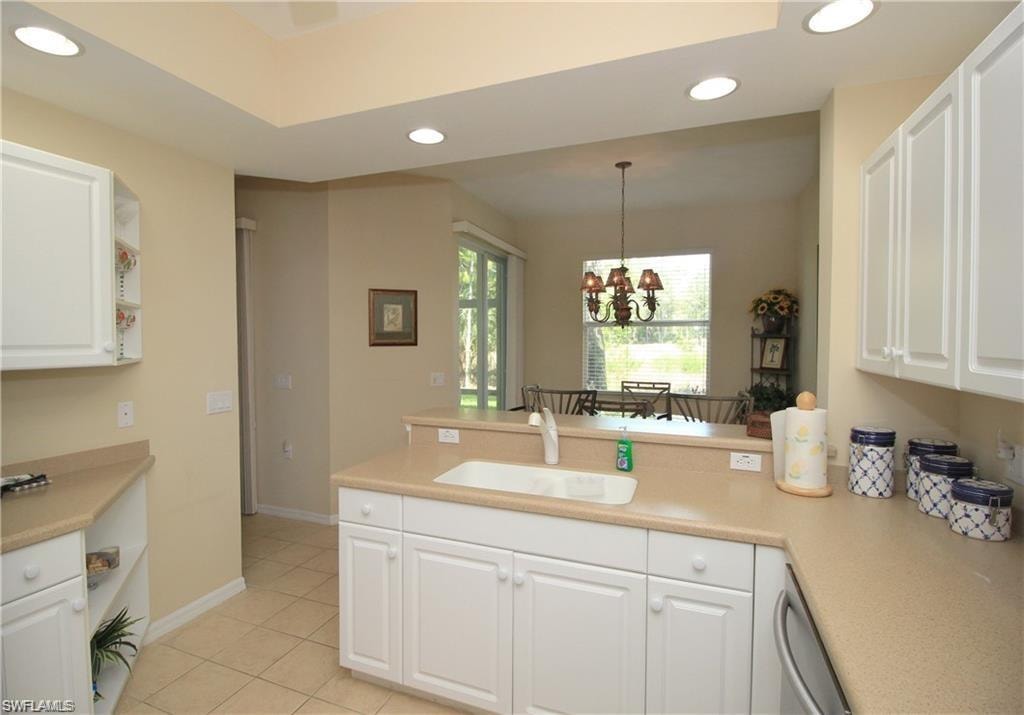 Kitchen with decorative light fixtures, kitchen peninsula, sink, a chandelier, and white cabinets