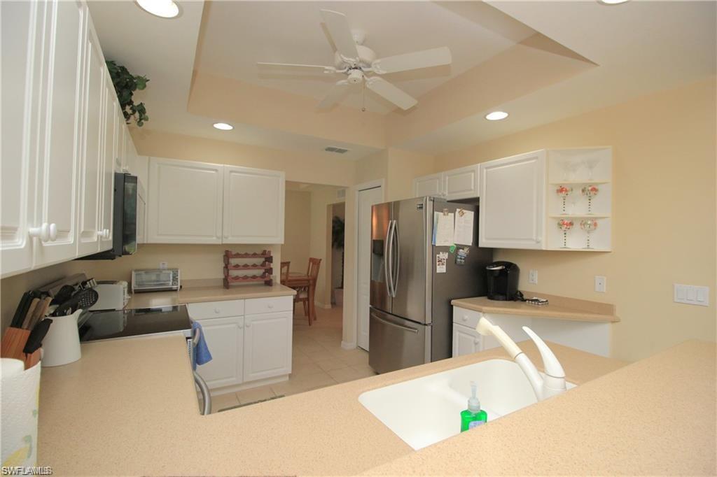 Kitchen featuring white cabinetry, sink, ceiling fan, stainless steel fridge with ice dispenser, and a raised ceiling