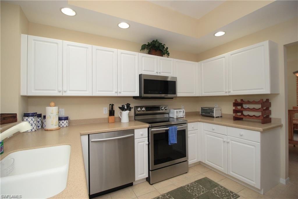 Kitchen featuring light tile patterned floors, stainless steel appliances, white cabinetry, and sink