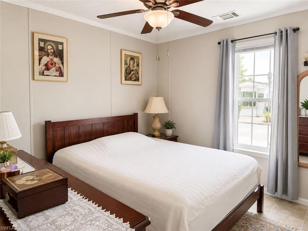 Bedroom featuring a ceiling fan with integrated lighting, a window with vertical grids, and neutral-toned wall paneling