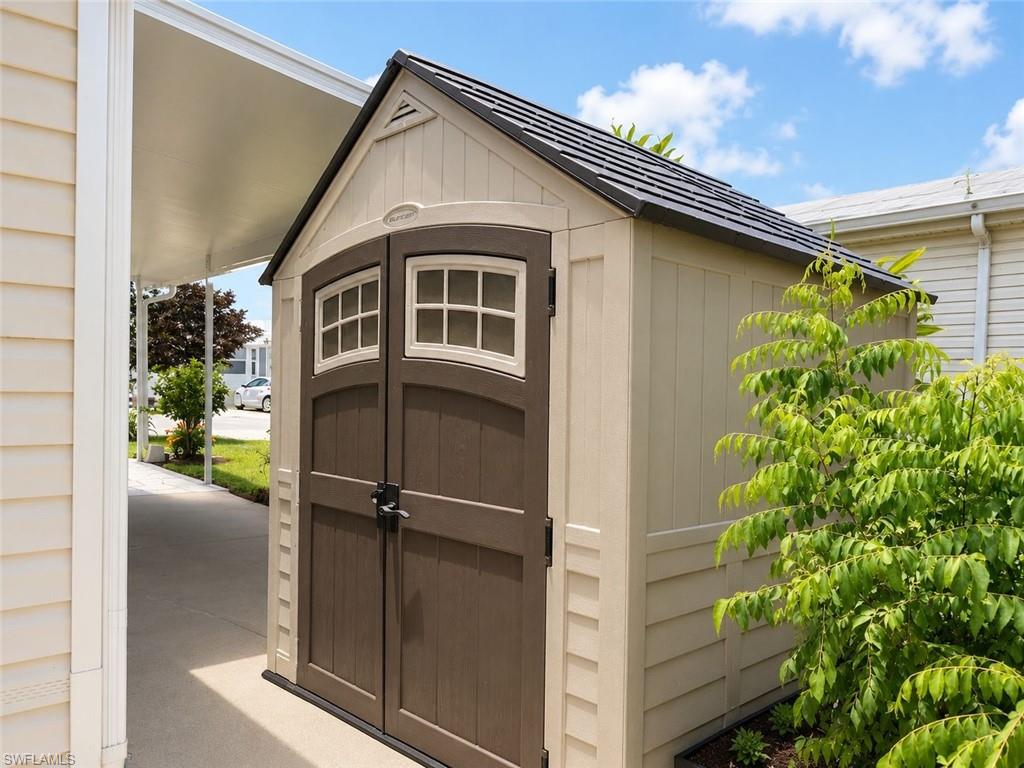 Exterior storage shed featuring a gabled roof, dual arched paneled doors with window accents, and light-toned siding
