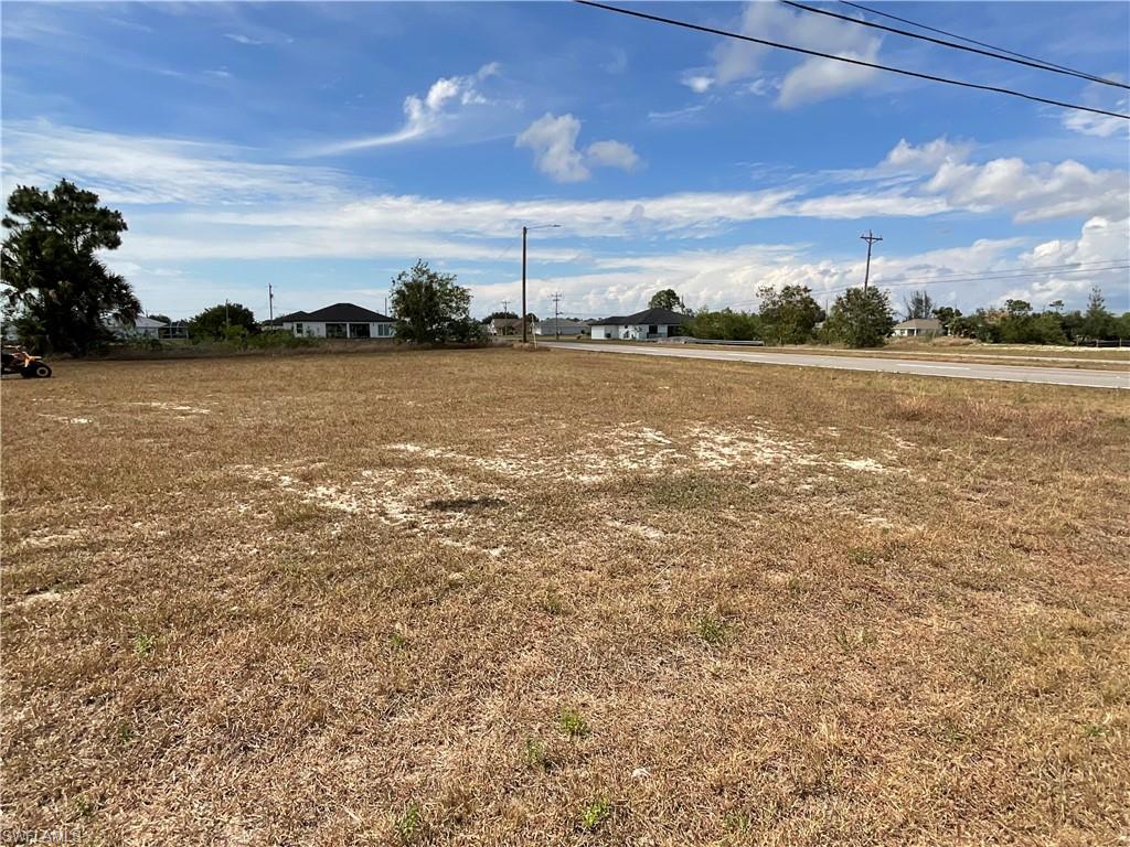 Expansive residential lot featuring a flat topography, established roadway, power lines, and distant single-story homes
