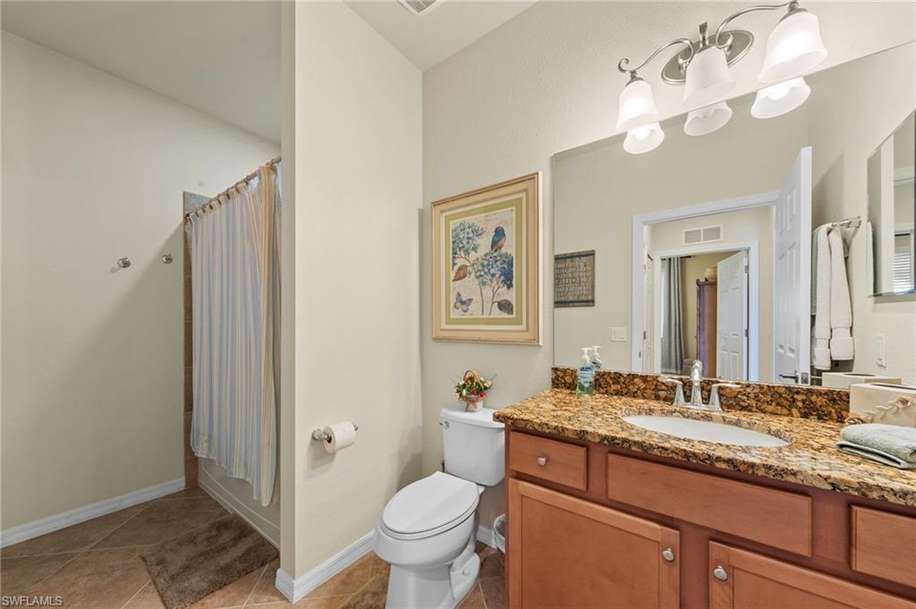 Bathroom featuring a wood-finish vanity with a granite-style countertop, undermount sink, and a multi-bulb vanity light fixture