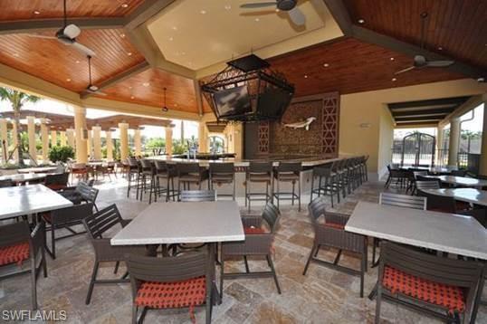 Expansive outdoor covered patio featuring a full-service bar with bar seating, multiple dining tables, wood-paneled ceilings with ceiling fans, and stone-finish flooring