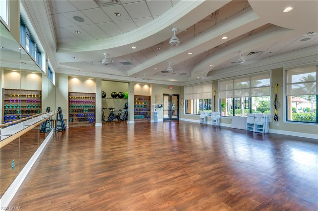 Spacious multi-purpose room featuring wood-finish flooring, mirrored wall with ballet barre, recessed lighting, and large windows with roller shades