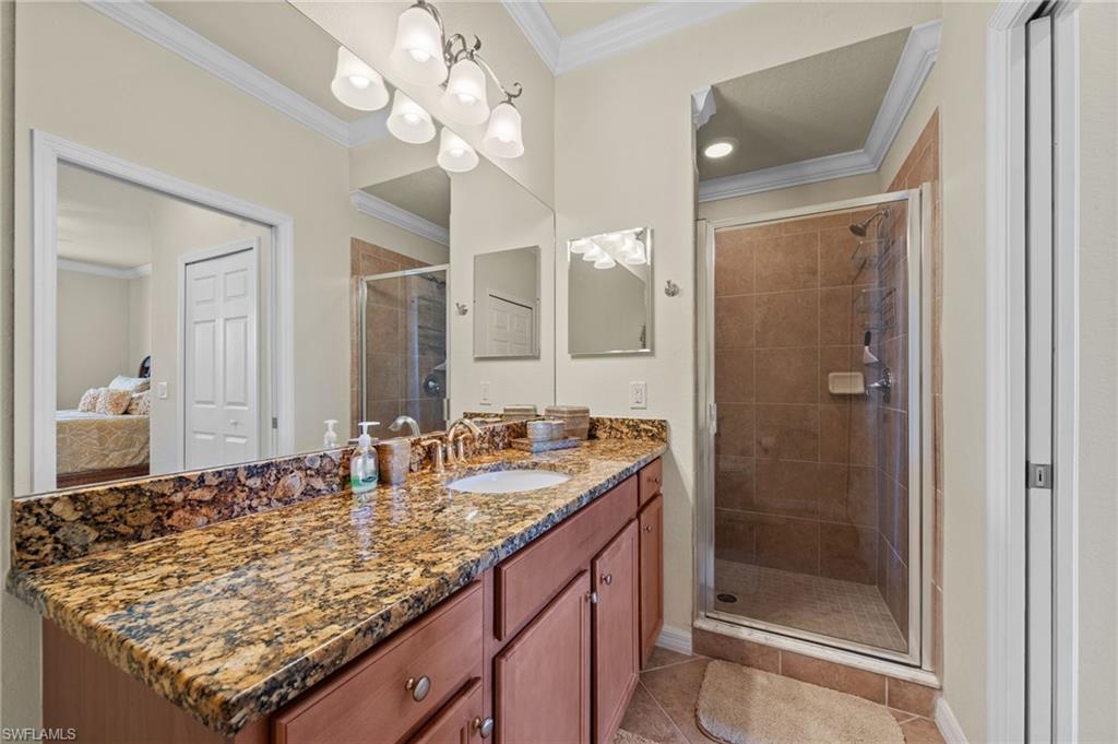 Bathroom with an expansive vanity featuring a stone countertop, an integrated sink with a polished brass-tone faucet, and a large wall-mounted mirror