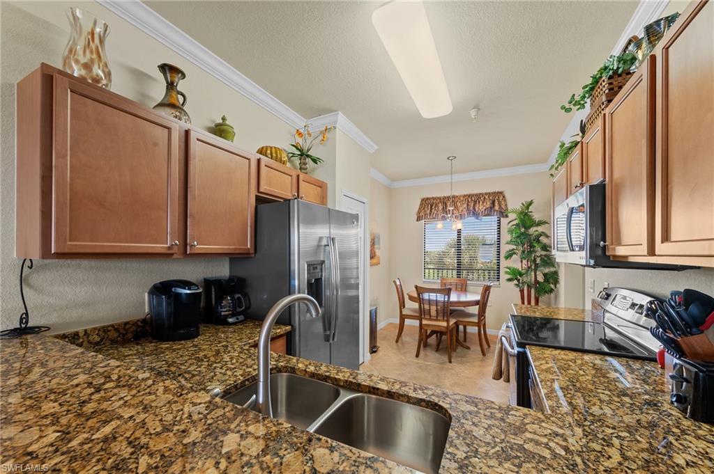 Kitchen featuring a double stainless steel sink, patterned stone countertops, wood-finish cabinetry, and stainless steel appliances