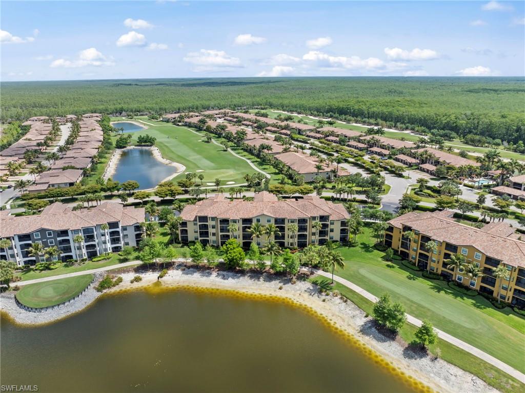 Expansive aerial showcasing a residential community with multiple multi-story buildings featuring terracotta-style roofs, a golf course with manicured greens, multiple water features, and extensive landscaping
