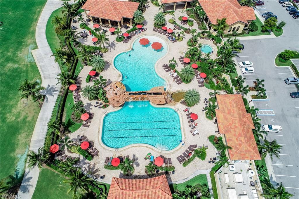 Expansive resort-style pool complex featuring two distinct swimming pools, a rock-detailed bridge, and multiple red-umbrella shaded lounge areas