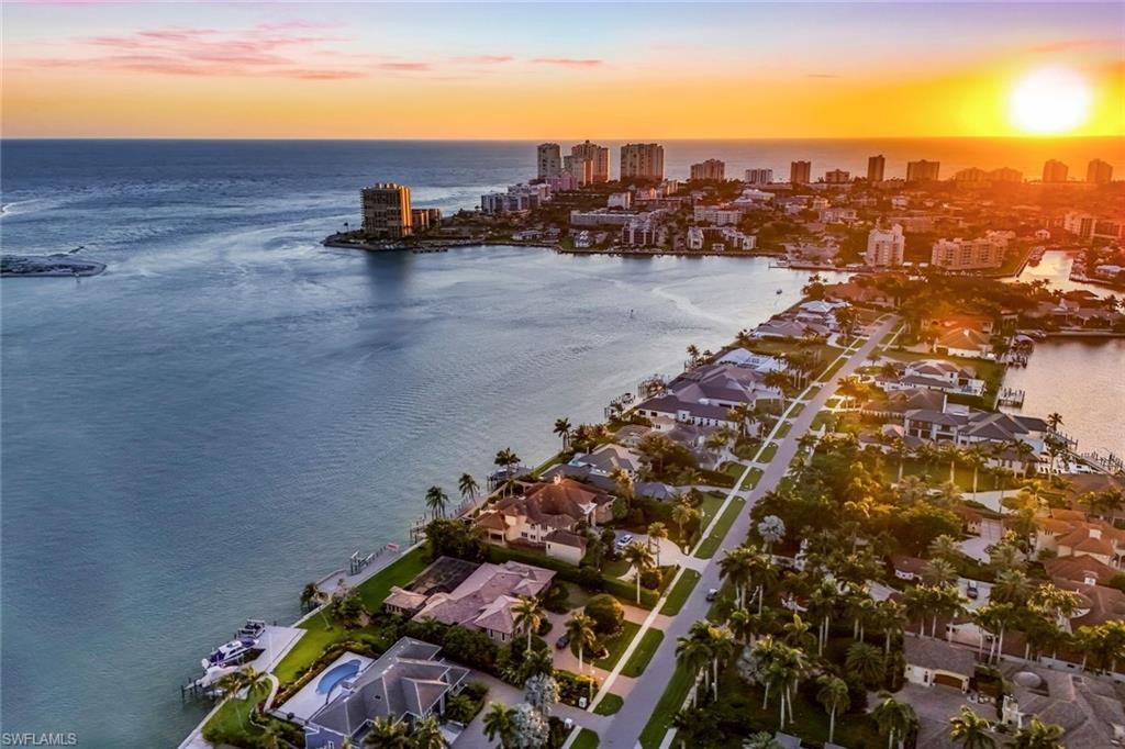 Aerial perspective showcasing waterfront properties with private docks, a palm-lined street, multiple residential structures, and distant high-rise buildings
