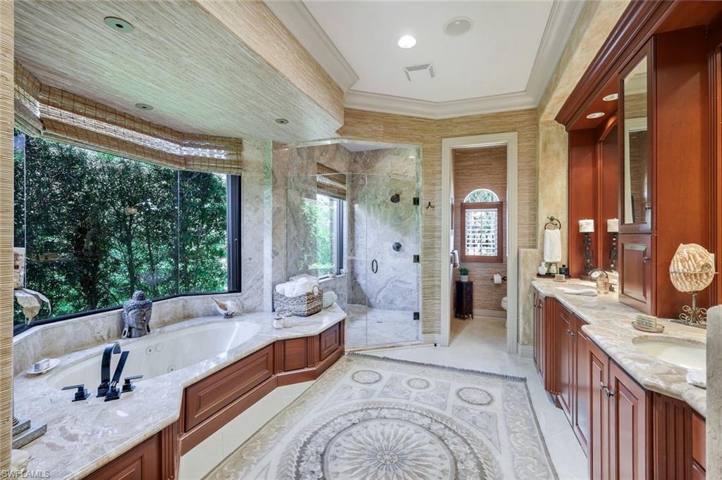 Spacious bathroom featuring a built-in jetted tub surrounded by large windows, a walk-in shower with glass enclosure, dual vanity with undermount sinks, and detailed mosaic tile flooring